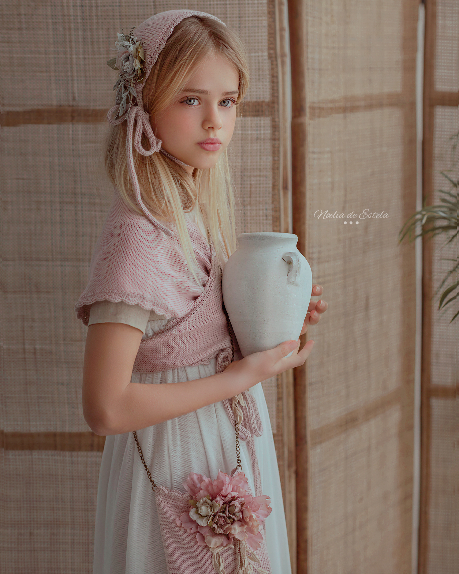 Retrato de Comunión con vestido blanco, complementos rosas y una jarra