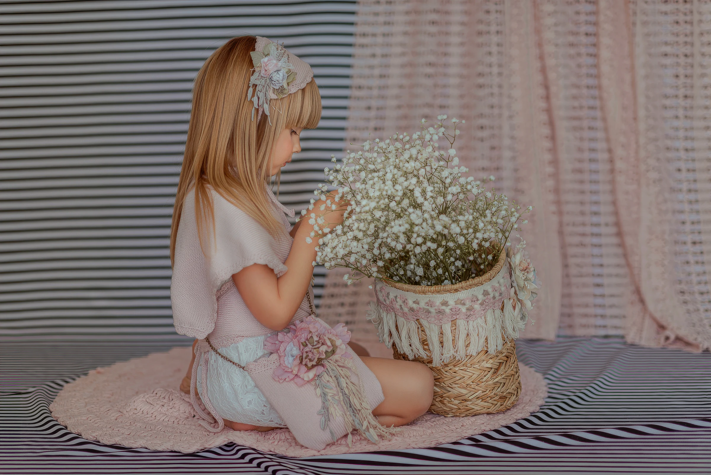 Niña junto a una cesta de flores en una escenografía rosa